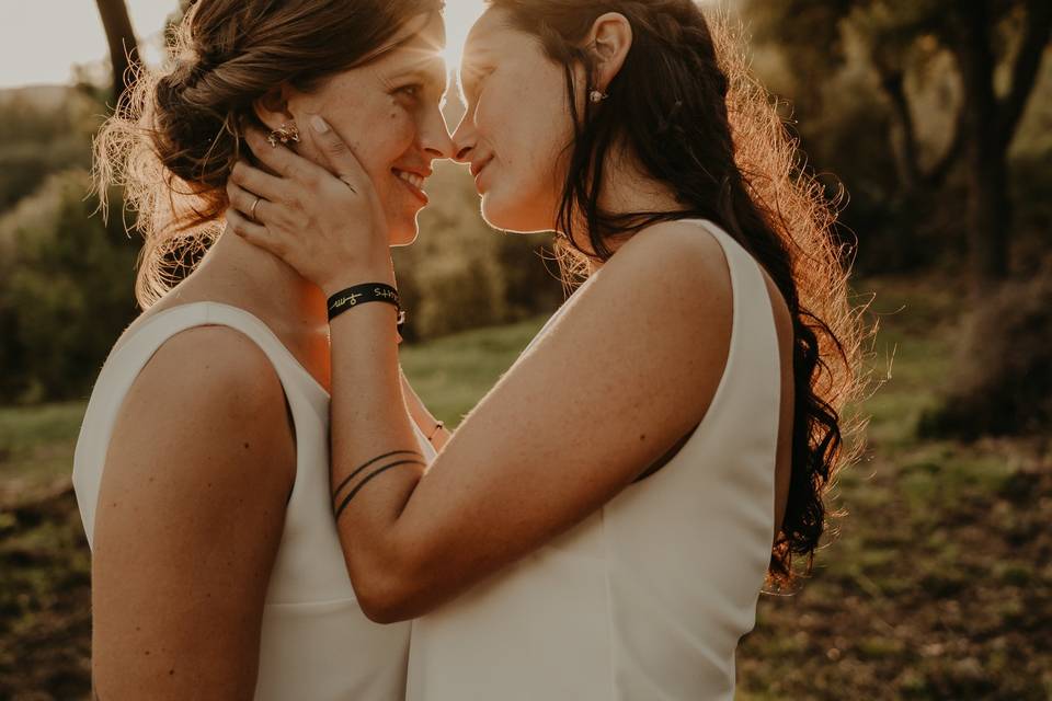 Dos chicas vestidas de novia se miran fijamente a los ojos mientras una le coge la cara a la otra y están a punto de besarse