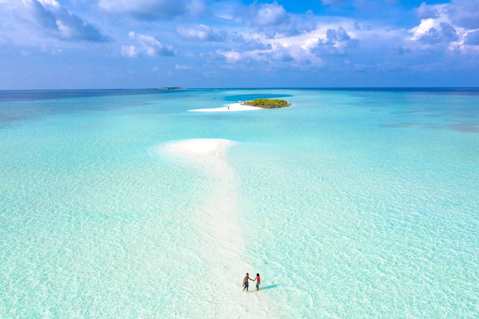 Pareja caminando cogida de la mano y rodeada por el océano en las Maldivas