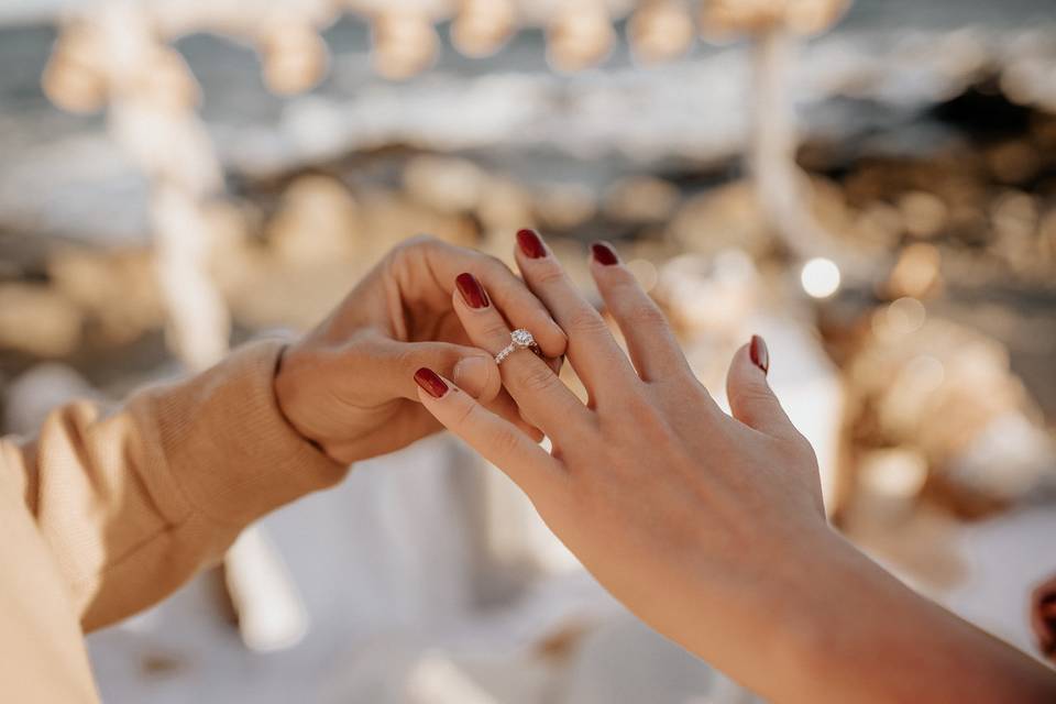 Mano de hombre poniéndole un anillo en el dedo a una mano de mujer con las uñas pintadas de color rojo