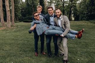 grupo de amigos con trajes modernos en medio del bosque levantando a uno de ellos