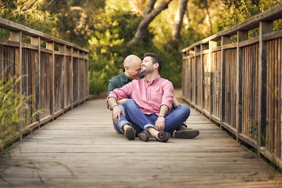 Pareja de dos chicos felices sentados en el suelo de un puente de madera