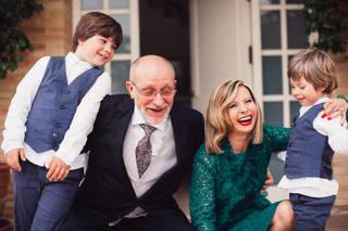 Bodas de oro: señor y señoras mayores, agachados, elegantes y muy sonrientes abrazan cada uno a un niño con chaleco azul y camisa blanca