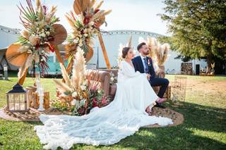 Novio y novia sentados en un sofá de aire vintage junto a dos estructuras triangulares de madera con hierba de la pampa y muchas flores