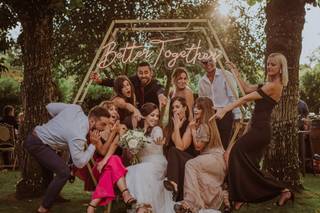 Grupo de amigos en un photocall con forma hexagonal mientras una chica vestida de novia enseña su anillo a todos los demás