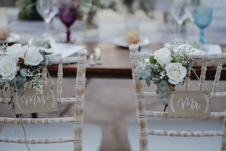 Sillas de los novios el día de la boda con pequeños carteles de Mr y Mrs y bonitos ramilletes de flores