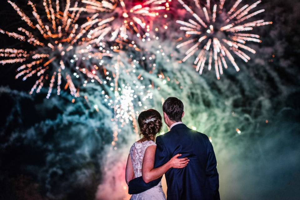 Pareja de recién casados mirando abrazados un castillo de fuegos artificiales por la noche
