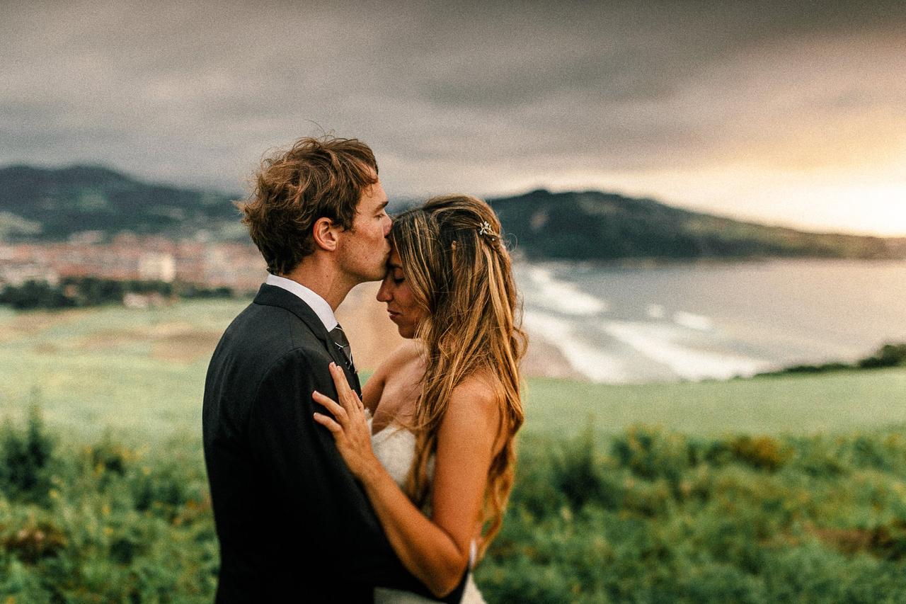 Pareja se abraza cariñosamente mientras él besa la frente de ella en un precioso lugar frente al mar