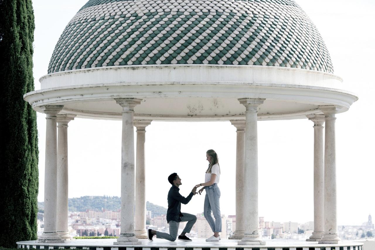 Formas originales de dar el anillo de compromiso: chico arrodillado delante de su pareja, con las manos cogidas, en un templete al aire libre