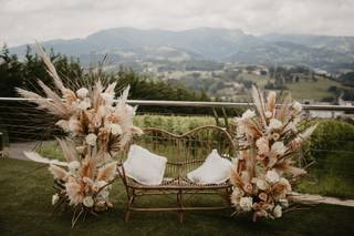 Decoración boda exterior: butaca doble con hierba de la pampa y otras flores y plantas alrededor