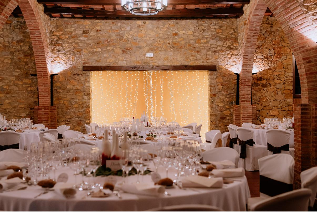 Masía rústica con salón boda, mesas redondas, arcos y luces colgantes cálidas