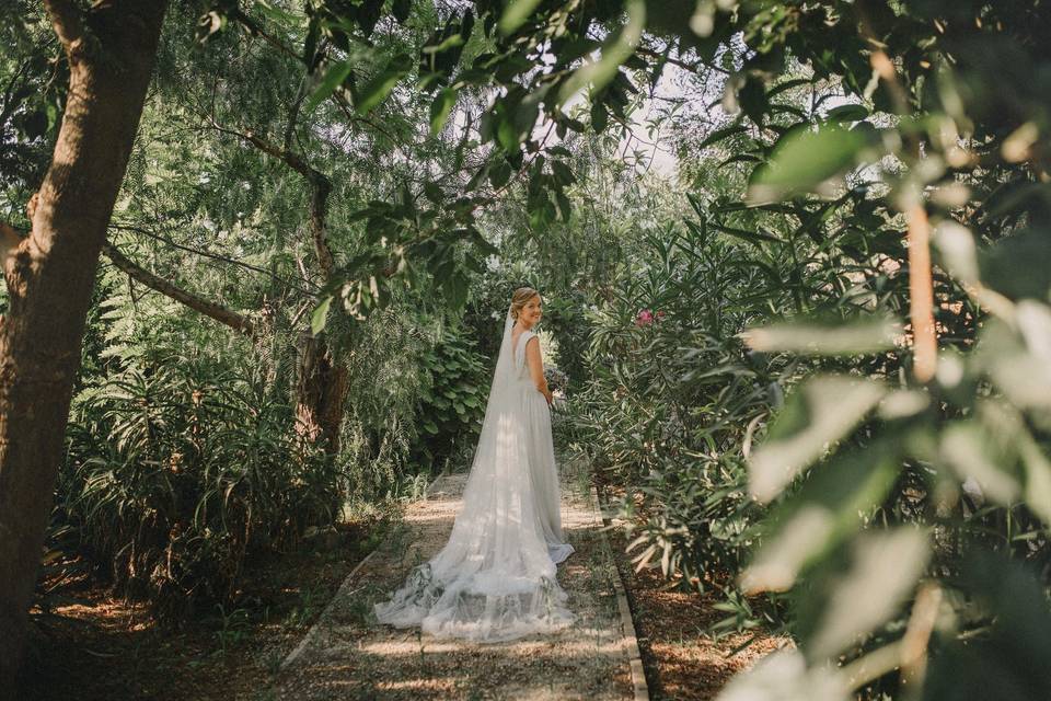Chica rubia sonriente con vestido y velo de novia en un jardín