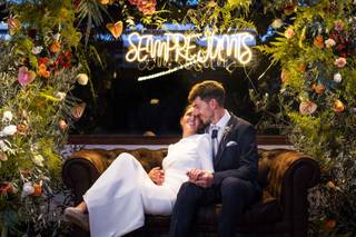 Pareja de recién casados sentados en un sofá debajo de un neón luminoso en el que pone 
