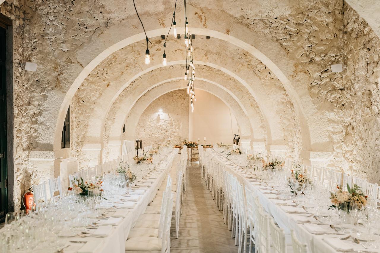 Espectacular ambiente interior todo en blanco con largas mesas horizontales preparadas para una comida o cena especial