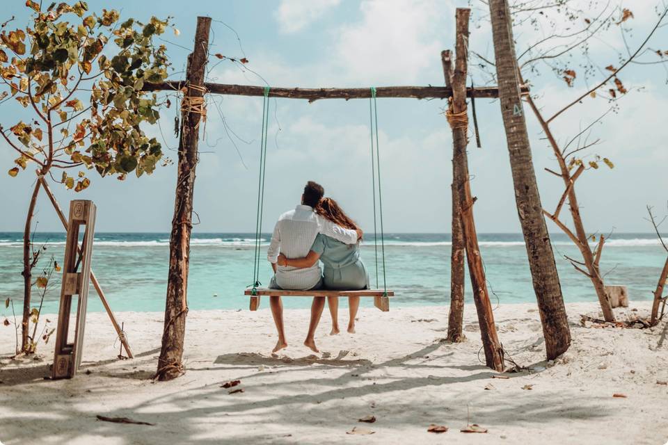 Pareja sentada en un columpio y abrazada en una playa paradisíaca de aguas turquesas