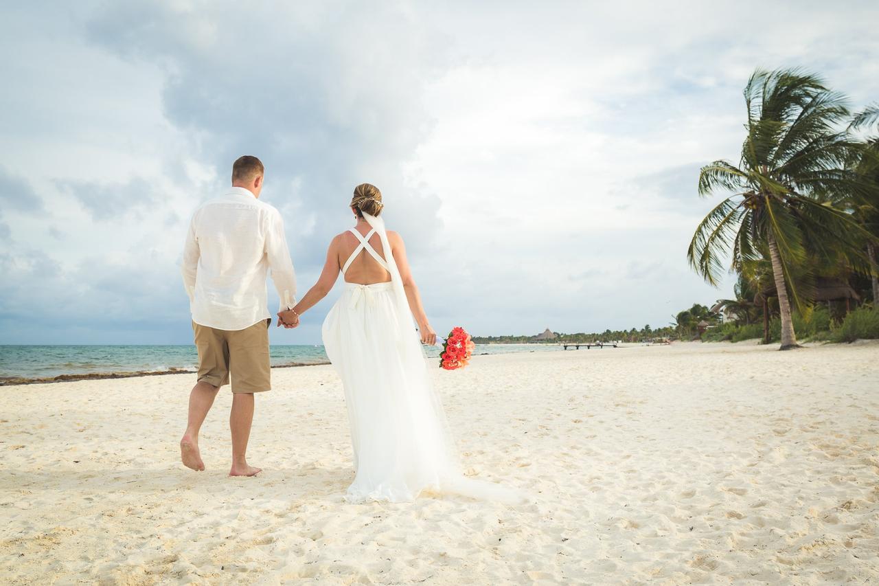 Pareja de espaldas caminando cogida de la mano por una preciosa playa con palmeras