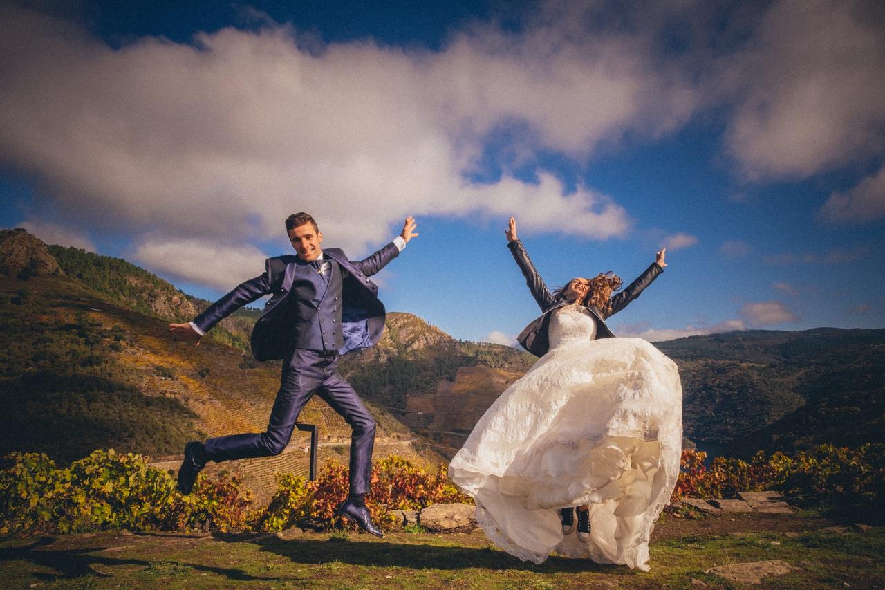 Chico con traje y chica con vestido de novia saltado con los brazos en alto en un ambiente al aire libre