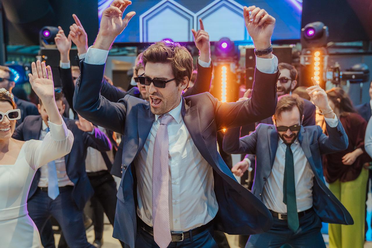 Canciones bailables en español: novia y chicos con traje y corbatas con gafas de sol bailando con los brazos levantados
