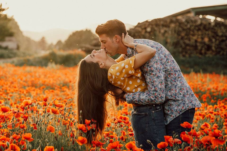 chico dándole un beso al cuello a una chica en medio de un campo con flores