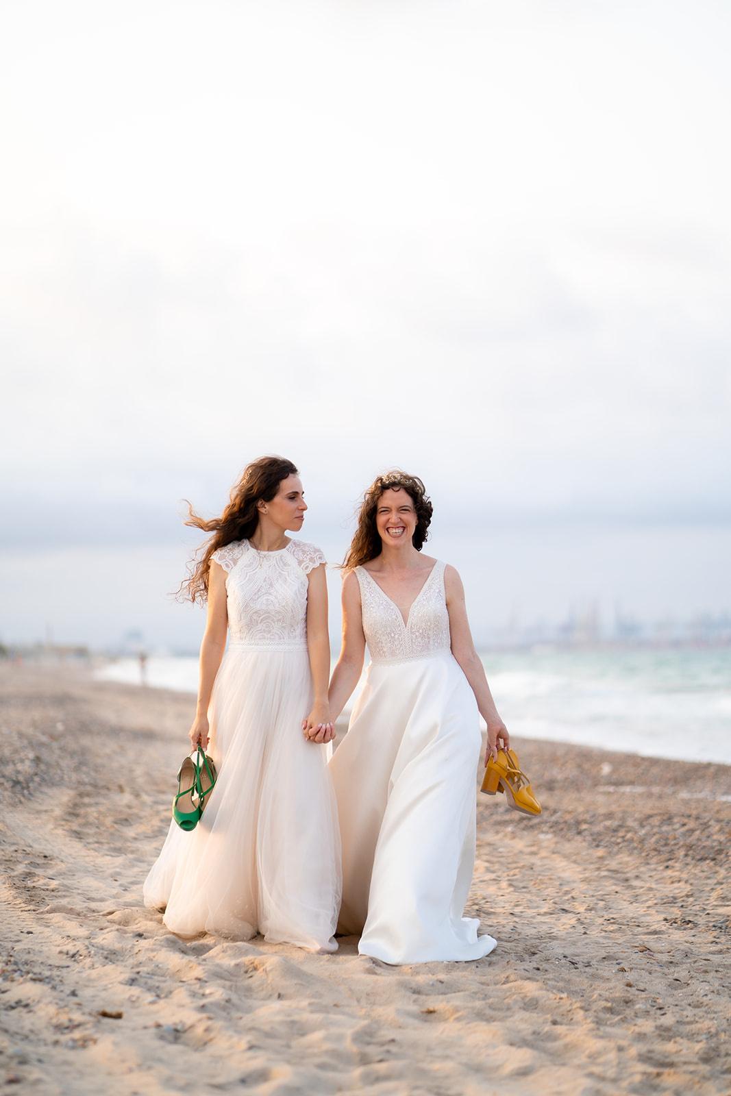 DDos chicas vestidas de novia caminan por la playa cogidas de la mano