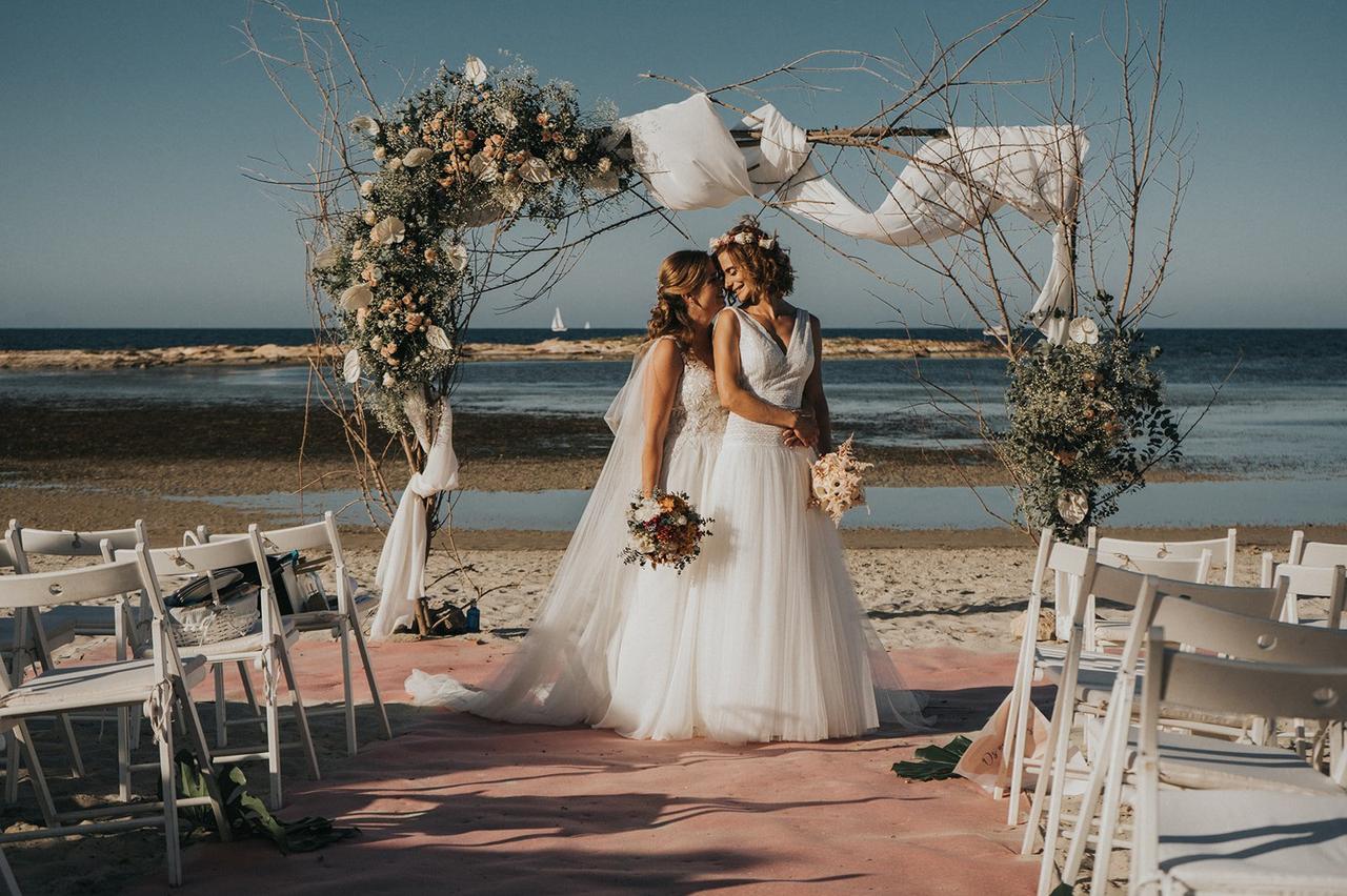 Dos chicas vestidas de novia se abrazan junto al altar de una ceremonia civil en la playa