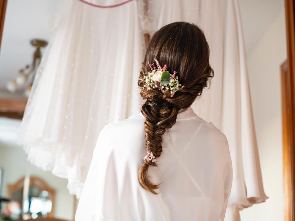 Peinado trenza: novia de espaldas con el pelo recogido en una trenza y adornado con flores