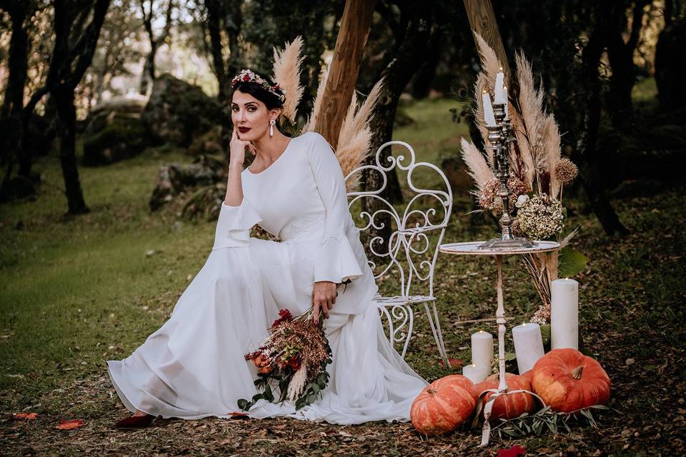 Chica vestida de novia sentada pensativa en un exterior con velas y calabazas como decoración