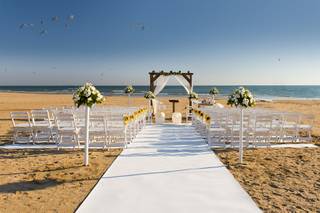 Playa con una gran alfombra blanca y sillas del mismo color preparada para una ceremonia civil al aire libre