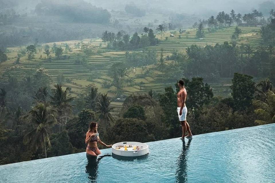 Chico y chica en una piscina desbordante con un magnífico paisaje asiático junto a ellos