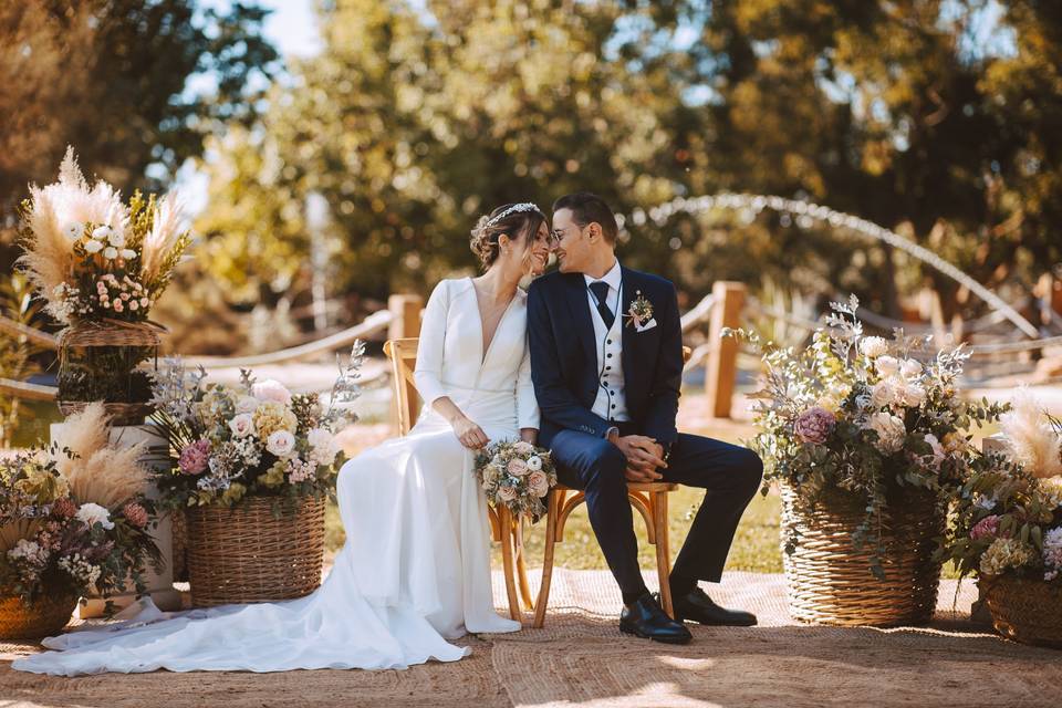 Cómo organizar una boda civil: pareja muy cariñosa sentada en unas sillas de madera en el altar de su ceremonia civil al aire libre