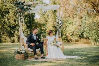 Pareja vestida de novio y novia durante la ceremonia civil al aire libre frente a una estructura de madera con telas y flores que da forma al altar