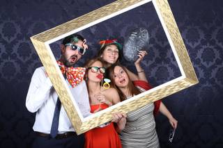 Amigos con varias piezas de atrezo se toman una divertida foto con un marco dorado en un photocall de boda