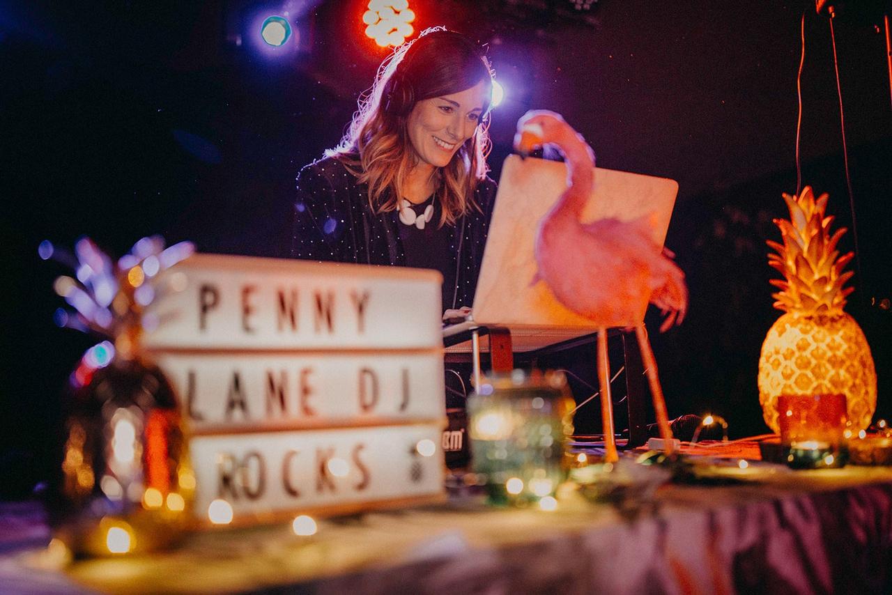 DJ de la empresa Penny Lane Djs trabajando en una boda sobre una mesa decorada con piñas y un cartel con letras luminoso