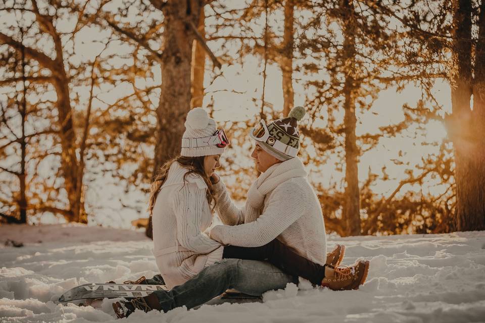 Planes de invierno en pareja: chico y chica sentados sobre la nieve con las piernas entrelazadas