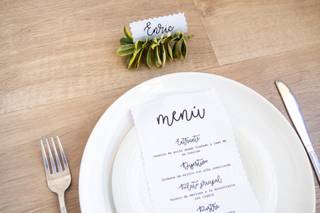 Mesa de madera con un plato blanco con un menú de tela encima y al lado una tarjeta con en la que hay escrito el nombre de Enric