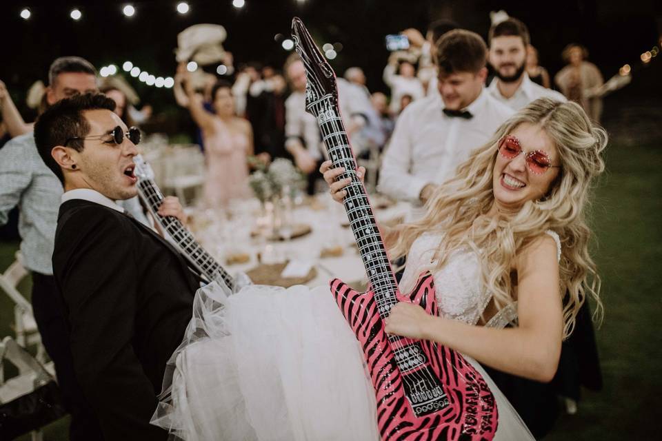 Canciones de rock de amor: pareja de recién casados toca divertida unas guitarras eléctricas de juguete al lado de algunos invitados a su boda