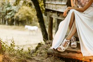 Chica sentada en una escalera de madera, en un exterior, con una falda lisa en color blanco y unas alpargatas blancas con lazo