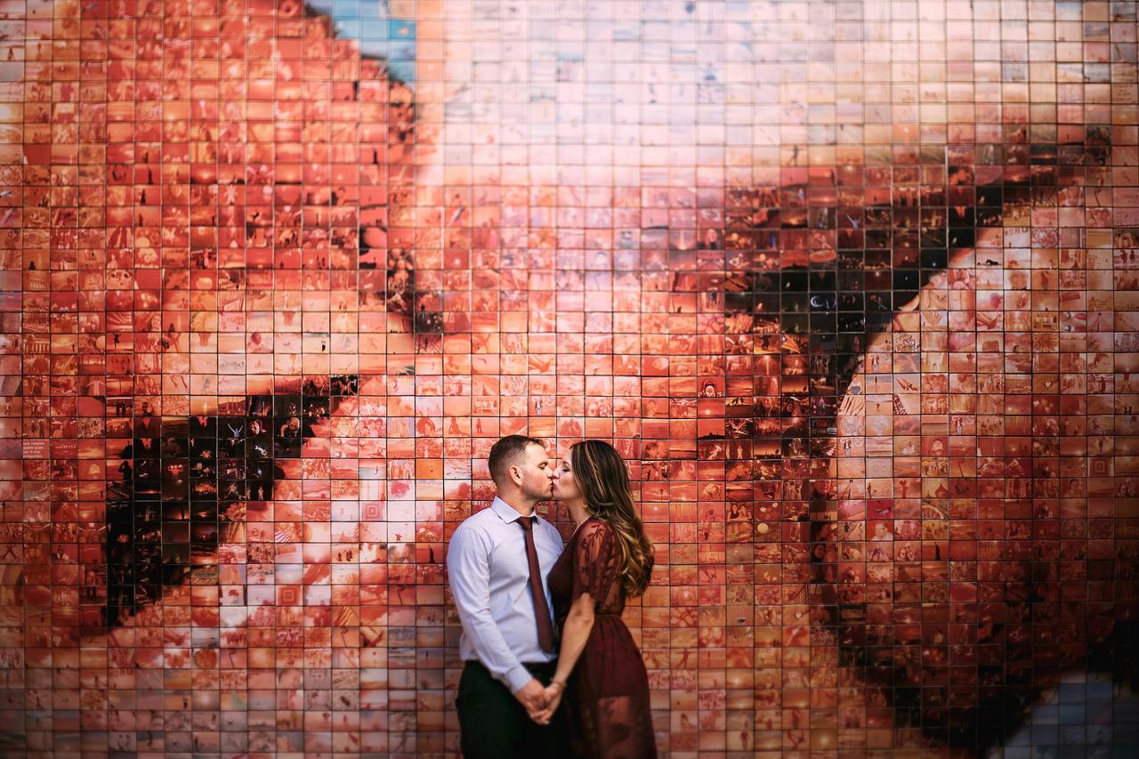 Dónde pedir matrimonio – en su sitio preferido: pareja con las manos cogidas se besa frente a un muro con la imagen de dos bocas besándose
