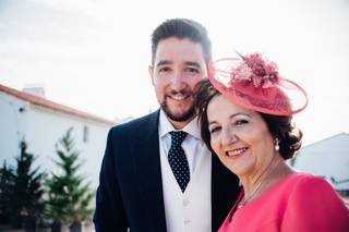 Madrinas de boda: novio y madrina con tocado a juego con el vestido fucsia posan muy sonrientes en un exterior