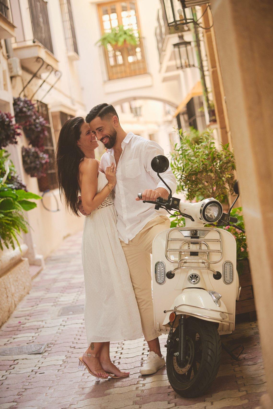 Pareja muy feliz y sonriente en una calle al lado de una Vespa