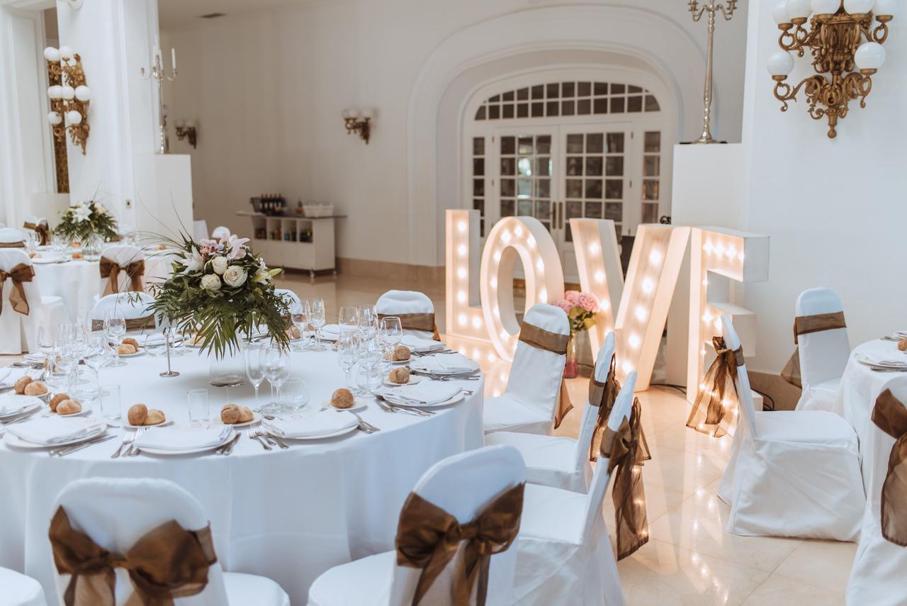 Salón con varias mesas y sillas vestidas de blanco y unas letras luminosas con la palabra LOVE