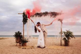 Casarse en la playa: pareja de recién casados con bengalas de colores en el altar de su boda en la playa