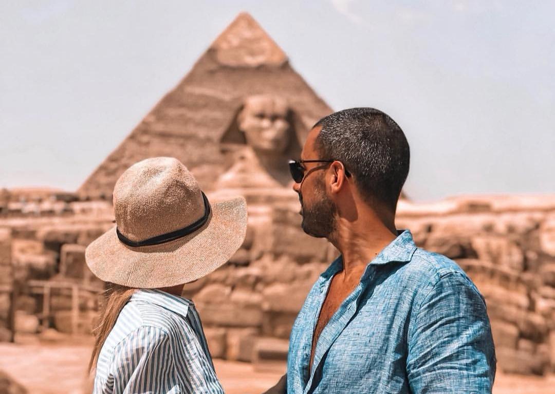 Chico y chica de espaldas frente a una de las pirámides de Egipto