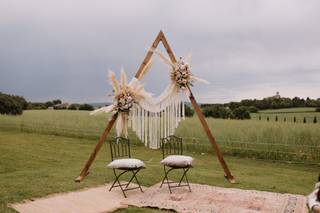 Estructura de madera de forma triangular con flores delante de dos banquetas en un exterior con césped