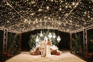 Iluminación bodas: precioso ambiente exterior con una pareja de novios de espaldas y una cuidada iluminación con lámparas y cielo estrellado