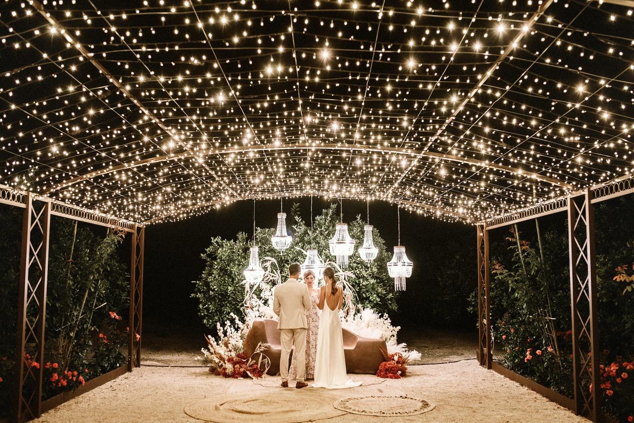Iluminación bodas: precioso ambiente exterior con una pareja de novios de espaldas y una cuidada iluminación con lámparas y cielo estrellado