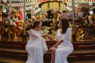 Ideas originales para bodas: dos chicas vestidas de novia sentadas delante de una atracción de caballitos