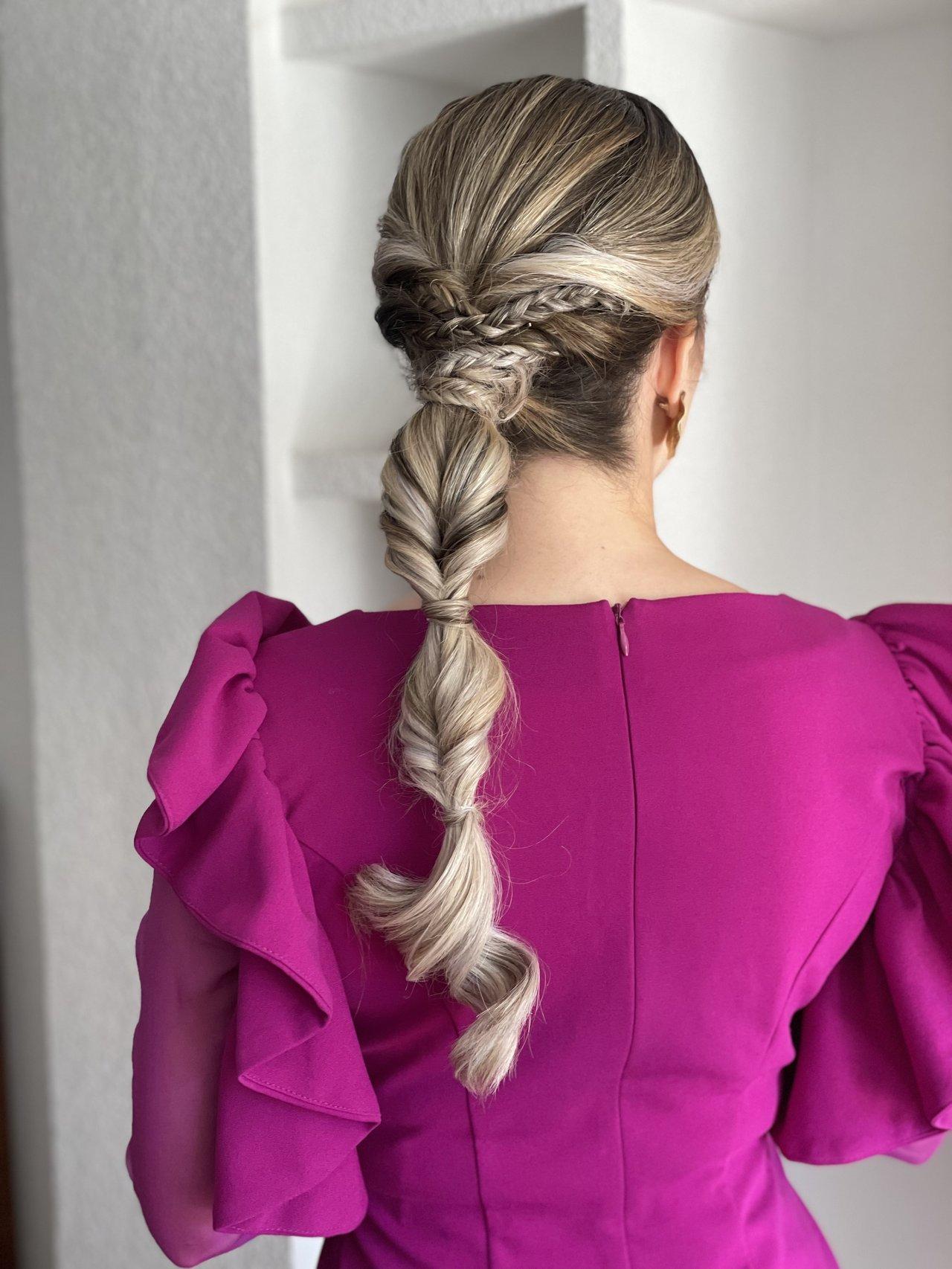 peinados trenzas boda: mujer rubia de espaldas con vestido color buganvilla y coleta combinada con trenzas en la parte superior