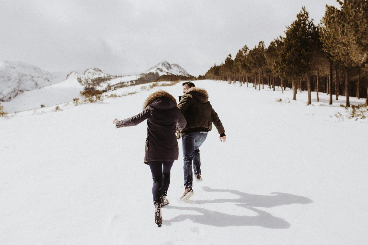 Planes de invierno en pareja: pareja cogida de la mano camina por la nieve