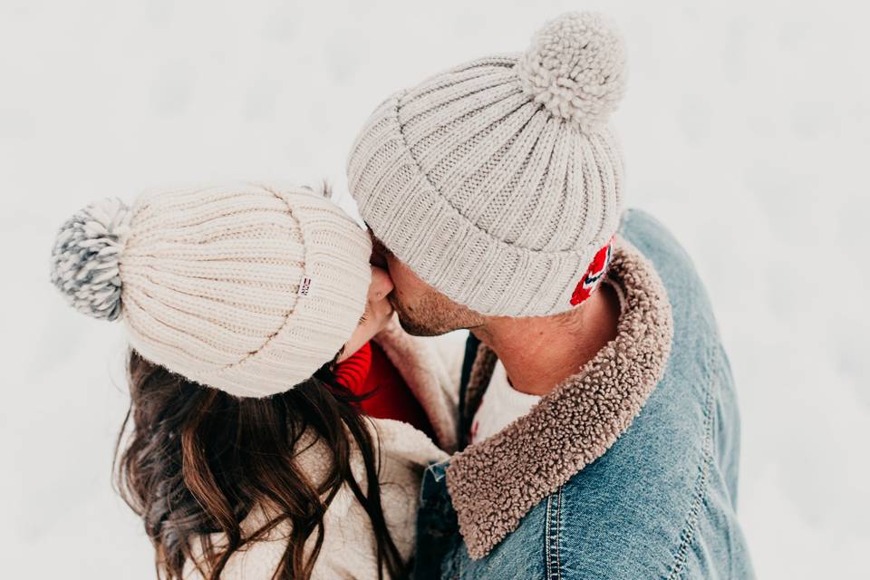 Pareja de chico y chica bien abrigados y con gorro de lana besándose