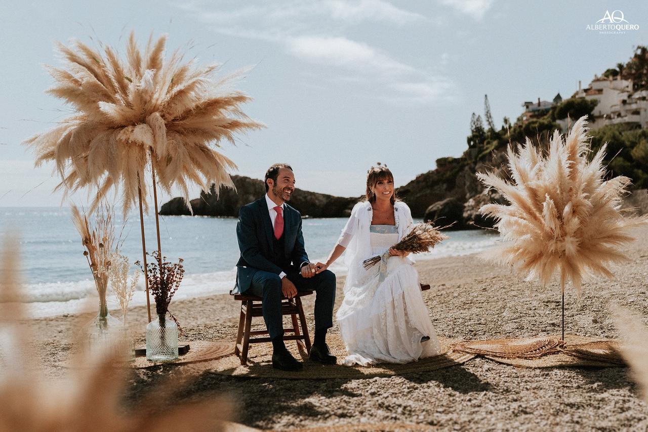 Pareja muy sonriente sentada en el altar de su boda civil en una playa